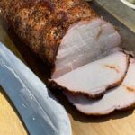 A Texas style smoked pork loin on cutting board with some slices.